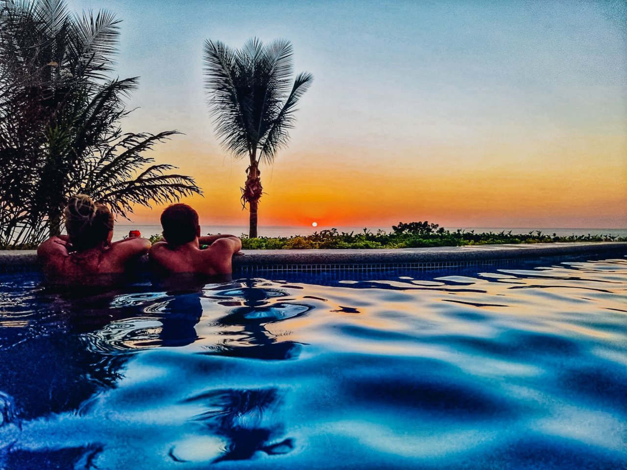 A couple watching the sunset in a pool overlooking the sea.